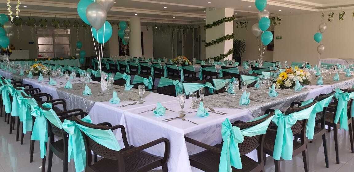 Une salle de banquet avec de longues tables, des housses de chaise de couleur turquoise et des ballons.