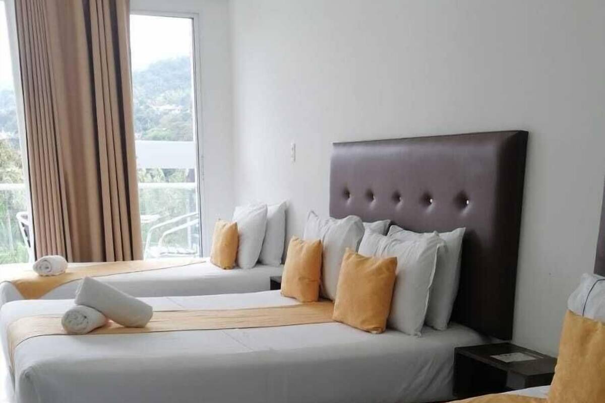 Hotellihuoneessa on kaksi sänkyä, joissa on valkoiset lakanat ja ruskea torkkupeitto. Huoneessa on suuri ikkuna, jossa on verhot, ja sen sisustus on moderni, ja sängynpääty on tumma.