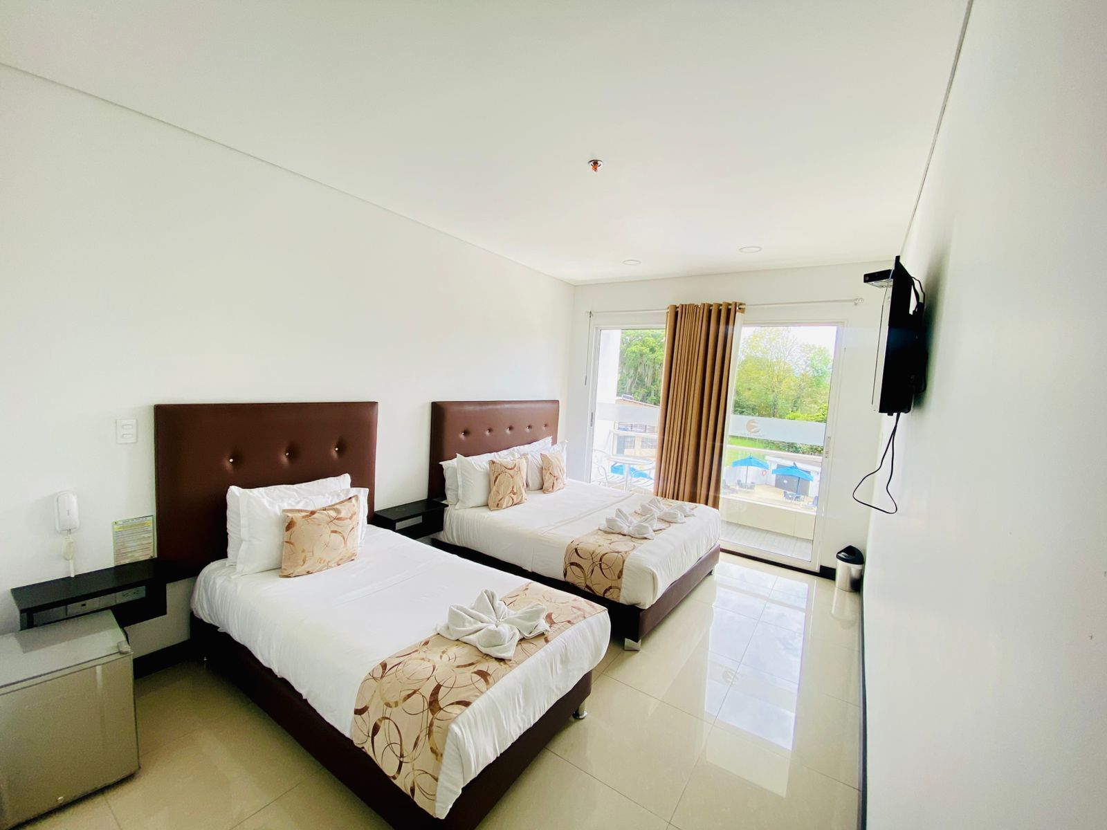 A hotel room with two beds, a flat-screen TV, and a view of the outdoors.