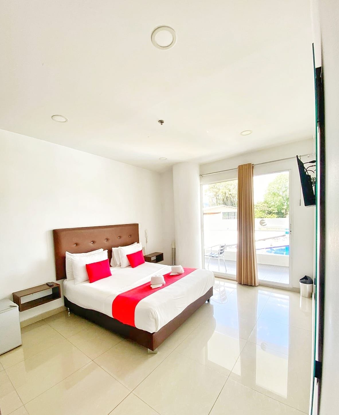 A modern hotel room with a large bed, a nightstand, a desk, and a view of the outdoors.