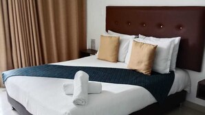 Une chambre d’hôtel avec un grand lit, une tête de lit sombre, du linge de lit blanc et une serviette roulée posée sur le lit.