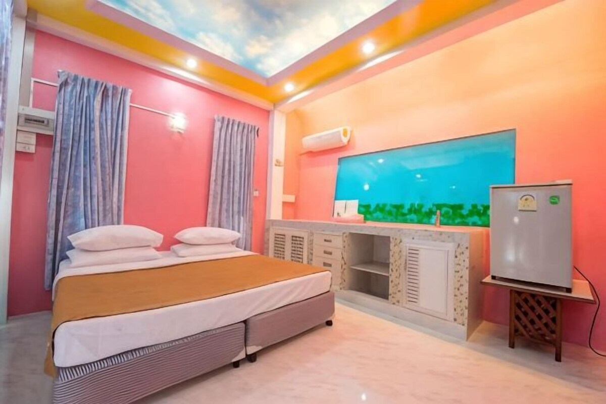 A bedroom with a bed, curtains, a TV, a refrigerator, and a window with a view.
