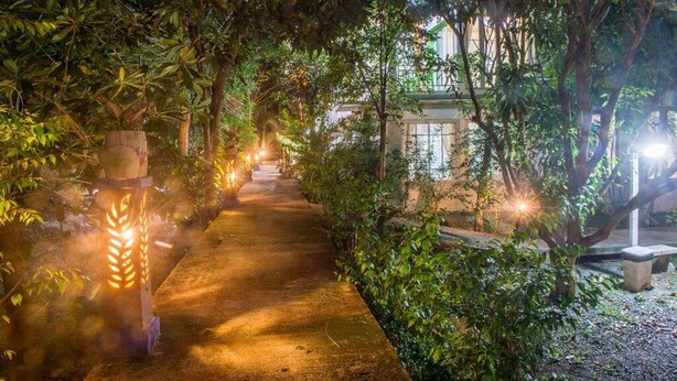 A pathway lined with trees and illuminated by soft lighting, leading to a building with large windows. - Poomvarin Resort (Nakhon Nayok)