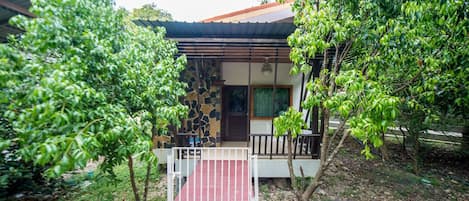 Une maison avec une façade en pierre, un chemin rouge menant à l’entrée et un petit porche doté d’une balustrade.