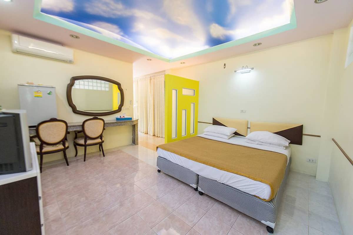 A hotel room with a bed, a desk, a chair, a mirror, and a ceiling with a sky design.