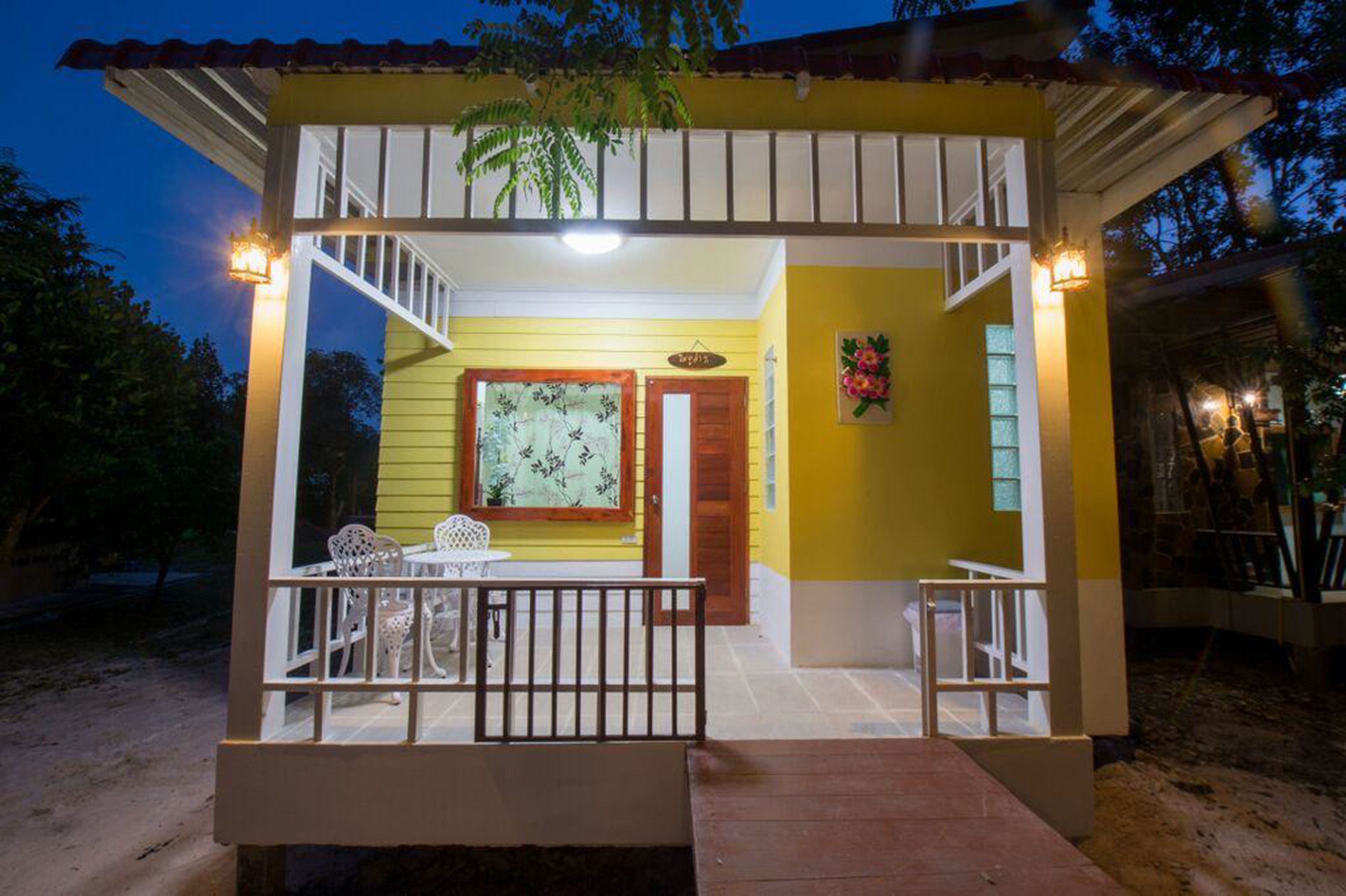 Um pequeno edifício amarelo com varanda coberta, porta de madeira e mesa com cadeiras.