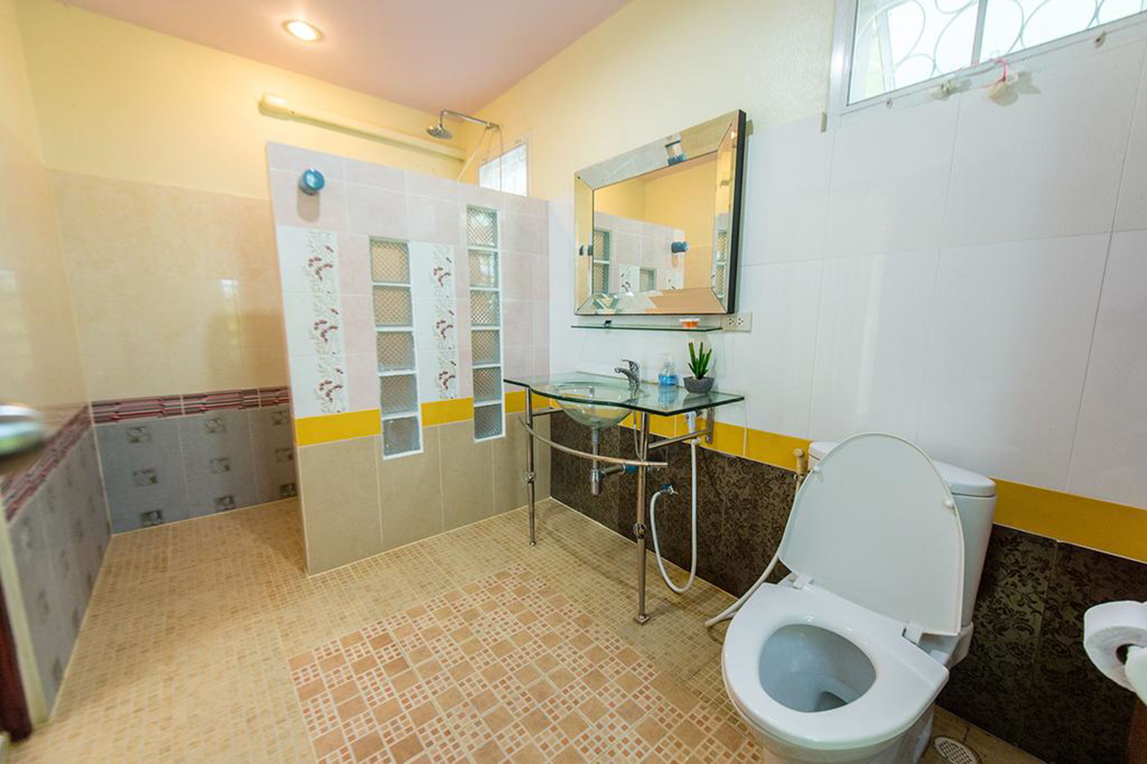 Un baño con lavabo de vidrio, inodoro y zona de ducha.