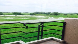 A balcony with a view of a green field and trees. - Nava Resort (Pak Phli)
