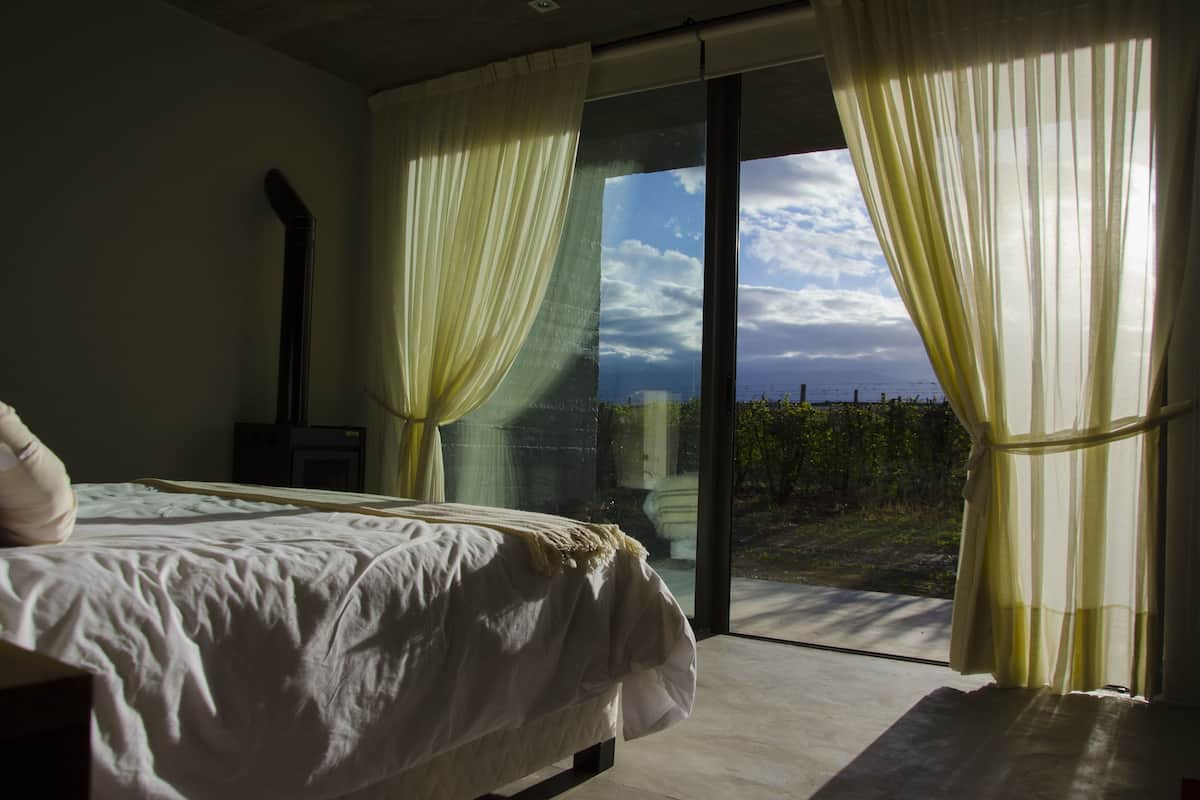 Une chambre à coucher avec un lit, une table de chevet et une grande fenêtre avec des rideaux.