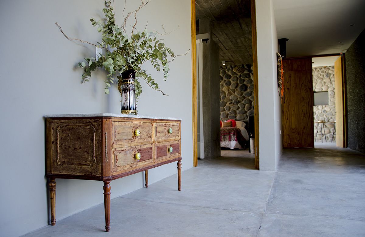 Un aparador de madera con cajones, un florero con follaje y una pared de piedra al fondo.