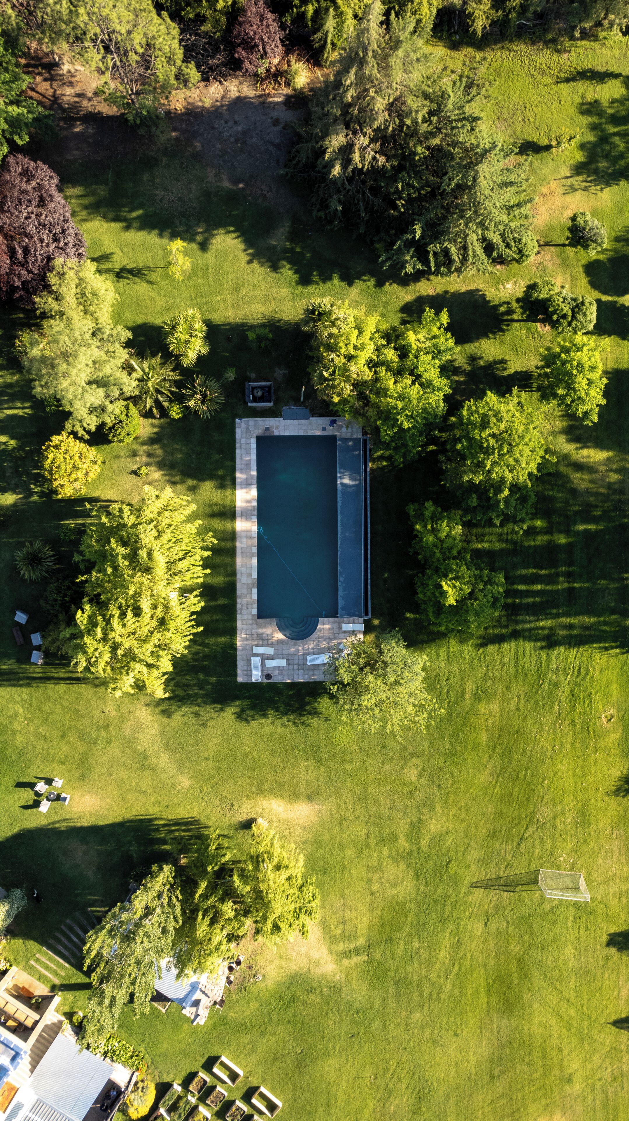 An aerial view of a property with a rectangular swimming pool, surrounded by a well-maintained lawn and trees.