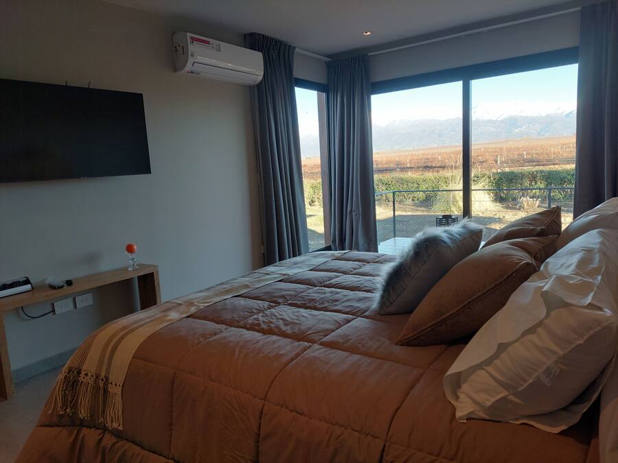 A bedroom with a large bed, an air conditioning unit, a TV mounted on the wall, and a view of a mountainous landscape through the window.