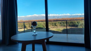 Ein Zimmer mit Tisch und einem Glas Wasser, Blick auf Berge und ein Weinberg.