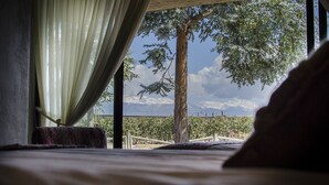 Ein Schlafzimmer mit Bett, einem Fenster mit Vorhängen und Blick auf Baum und Berge.
