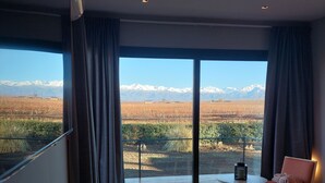 Ein modernes Hotelzimmer mit einer großen Glasschiebetür, die auf einen Balkon führt, einem Bett, einem kleinen Tisch mit einer Glasdekoration und einem Sessel.