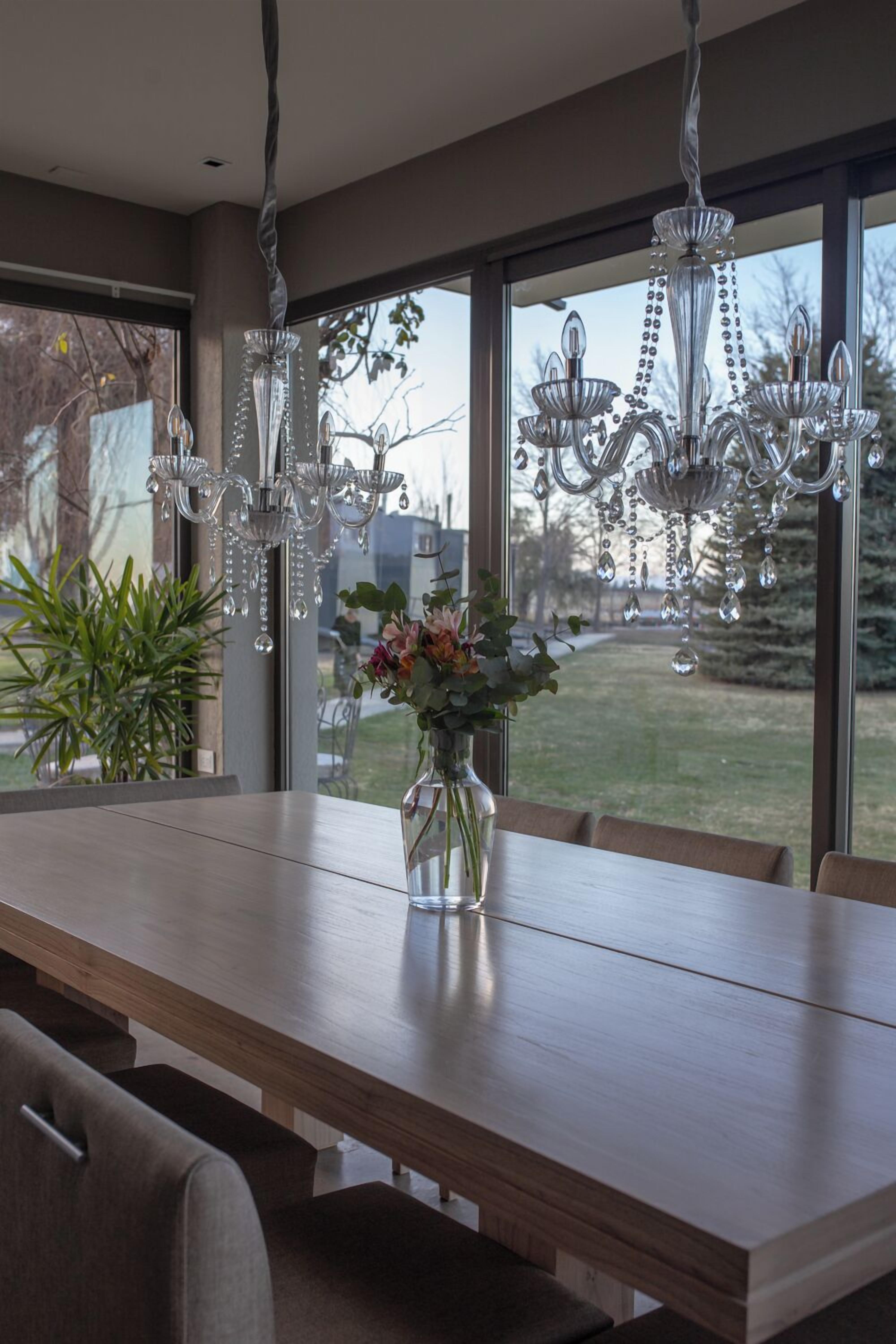 A dining area with a long wooden table, multiple chairs, a vase with flowers, and a chandelier.