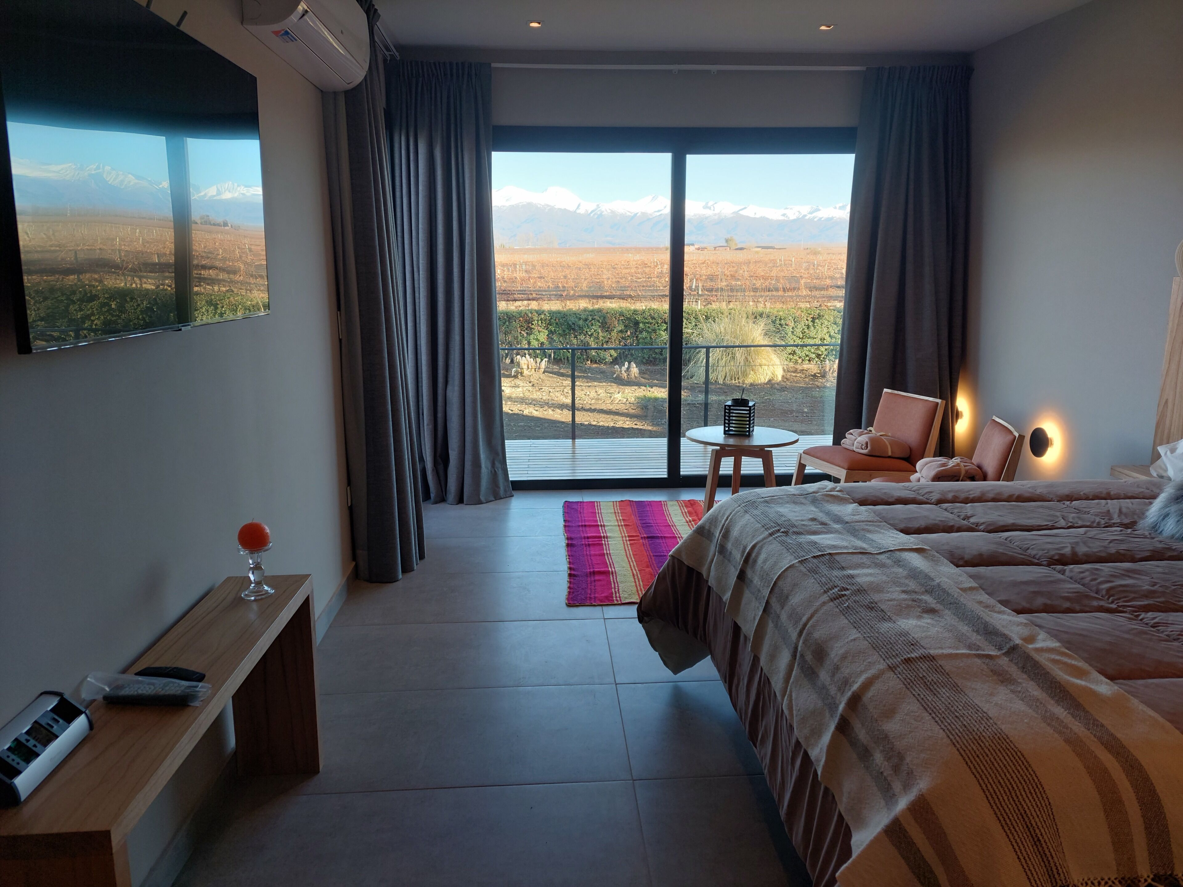 A hotel room with a large window, a bed, a chair, a small table, and a bench.