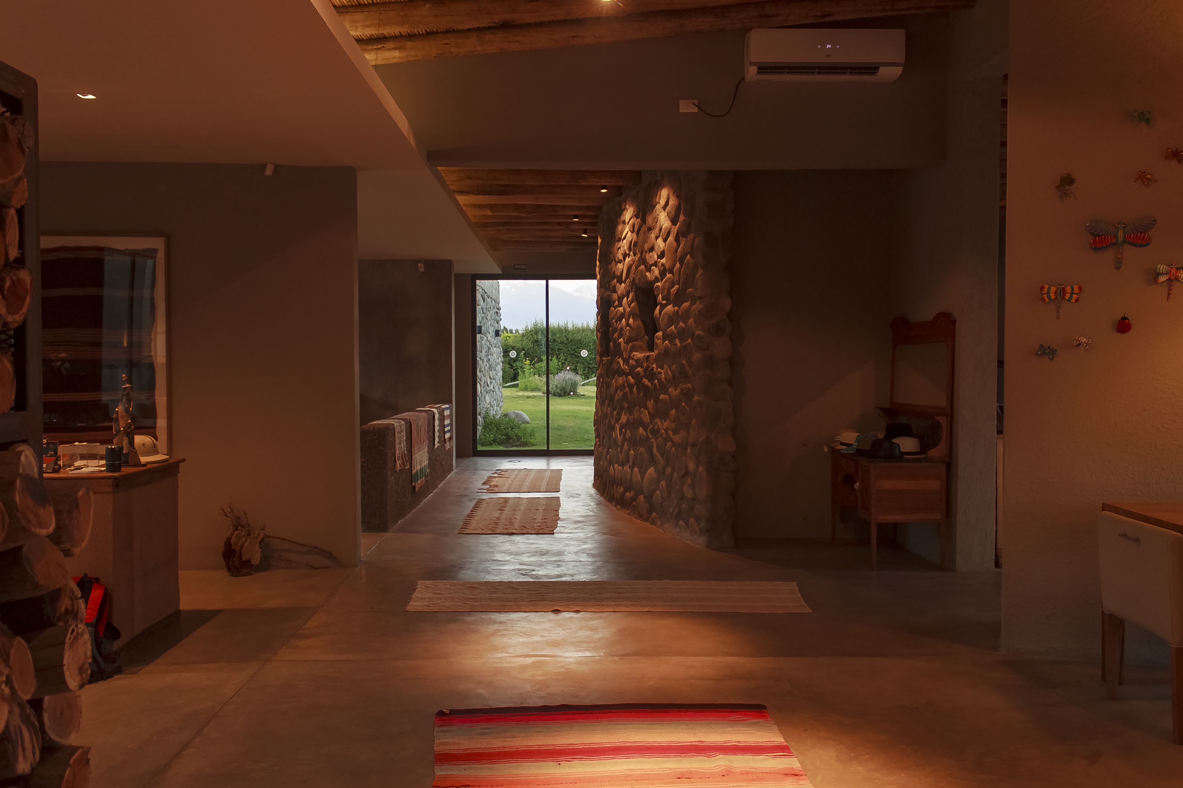 Een modern interieur met een stenen muur, een houten plafond en een uitzicht door glazen deuren op een buitenplaats.