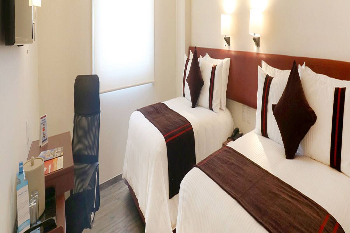 Une chambre d’hôtel avec deux lits, un bureau avec une lampe et une chaise.