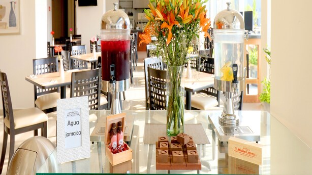 A hotel reception area with a glass counter displaying a beverage dispenser, a vase with flowers, and a sign indicating the hotel name. - Hotel Misión Express San Luis Potosí (San Luis Potosi)
