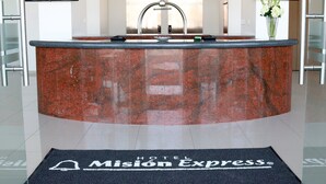 A reception desk with a marble top, two monitors displaying the hotel name, and a welcome mat with the hotel's logo. - Hotel Misión Express San Luis Potosí (San Luis Potosi)