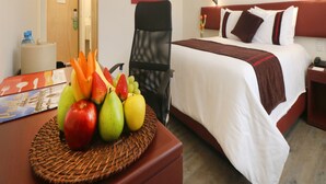 A hotel room with a neatly made bed, a desk with a fruit basket, and a chair. - Hotel Misión Express San Luis Potosí (San Luis Potosi)