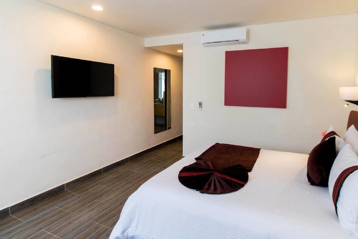 Une chambre d’hôtel avec un lit, un téléviseur à écran plat fixé au mur, un mur d’accent rouge et un couloir menant à une autre pièce.