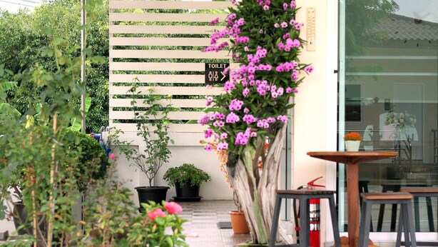 Un patio con plantas en macetas, una mesa de madera y un letrero que indica un baño.
