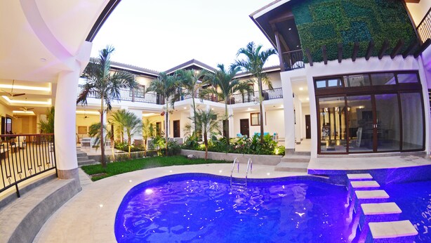 A swimming pool with steps leading into it, surrounded by a landscaped area with palm trees and a building with balconies. - Hotel Gran Balcón (Granada)