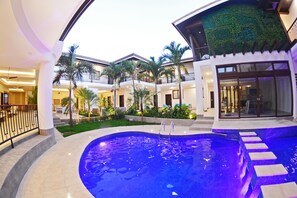 A swimming pool with steps leading into it, surrounded by a landscaped area with palm trees and a building with balconies. - Hotel Gran Balcón (Granada)