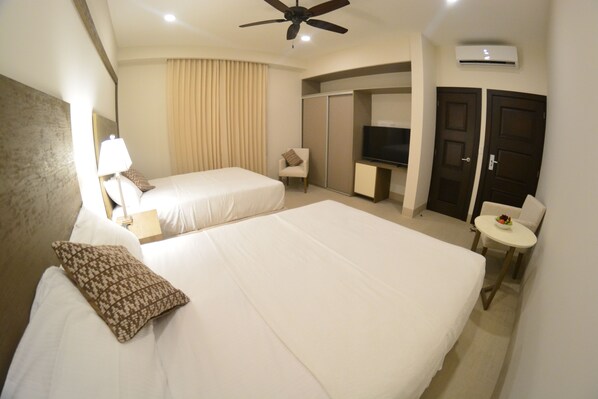 A hotel room with two beds, a TV, a small table with a bowl of fruit, a chair, and an air conditioning unit. - Hotel Gran Balcón (Granada)