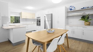 A modern kitchen with white cabinetry, a wooden dining table, and a built-in oven. - Aria Del Mare (Coolangatta)