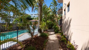 A pathway leading to a pool surrounded by palm trees and a building with a balcony. - Aria Del Mare (Coolangatta)