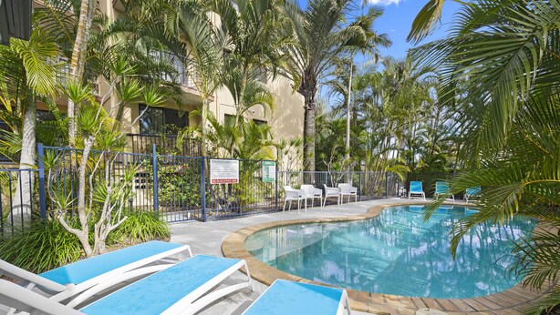 A pool area with lounge chairs, palm trees, and a sign indicating amenities. - Aria Del Mare (Coolangatta)