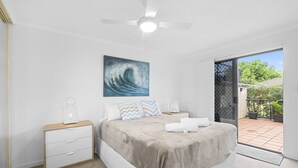 A bedroom with a bed, bedside tables, a ceiling fan, a painting, and a view of the outside. - Aria Del Mare (Coolangatta)