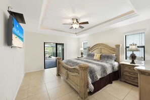 A bedroom with a bed, a ceiling fan, a TV, a window, and a nightstand.