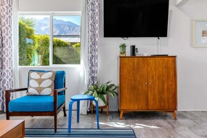 Quarto com sofá azul, uma pequena mesa, um armário, uma planta em vaso e uma TV fixada na parede.
