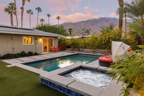 A swimming pool with a hot tub, surrounded by palm trees and a mountain view.