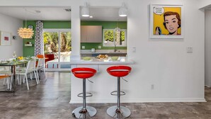 Une cuisine moderne avec un mur d’accent vert, deux tabourets de bar rouges et une œuvre d’art pop encadrée.
