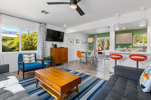 Ein modernes Wohnzimmer mit Sofa, Couchtisch, Fernseher und einem Essbereich mit Stühlen und Tisch.