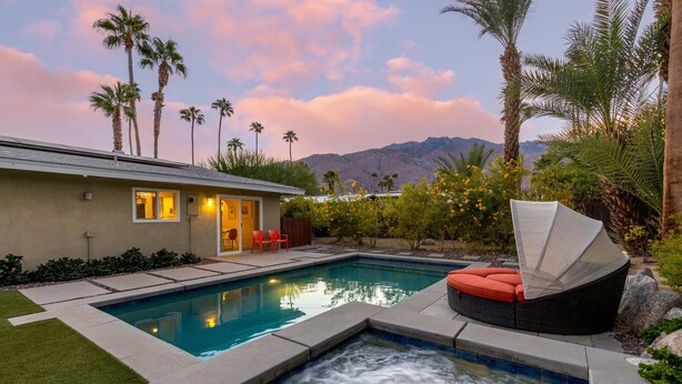 Une piscine avec un jacuzzi, une maison dotée d’une terrasse et des palmiers.