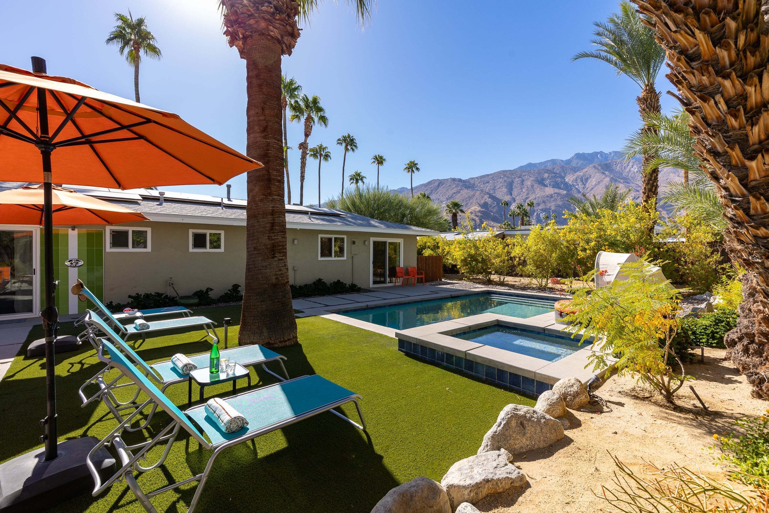 A pool area with artificial grass, lounge chairs, and a view of mountains.
