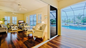 A spacious living room with a large sliding glass door leading to an outdoor deck. - Waterfront Paradise | Pool, Spa, Kayaks & Dock (Cape Coral)
