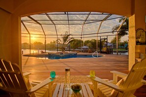 A wooden deck with a pool, chairs, and a table with drinks and a bowl of fruit. - Waterfront Paradise | Pool, Spa, Kayaks & Dock (Cape Coral)