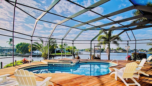 A covered outdoor swimming pool with wooden decking and Adirondack chairs. - Waterfront Paradise | Pool, Spa, Kayaks & Dock (Cape Coral)