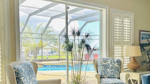 A living room with wicker furniture, a view of a pool, and a glass door leading outside. - Waterfront Paradise | Pool, Spa, Kayaks & Dock (Cape Coral)