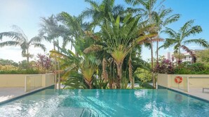 A swimming pool with clear water, surrounded by palm trees and other tropical plants. - Hemingway 3 Bedroom Condo 2 Blocks from the Beach (Deerfield Beach)