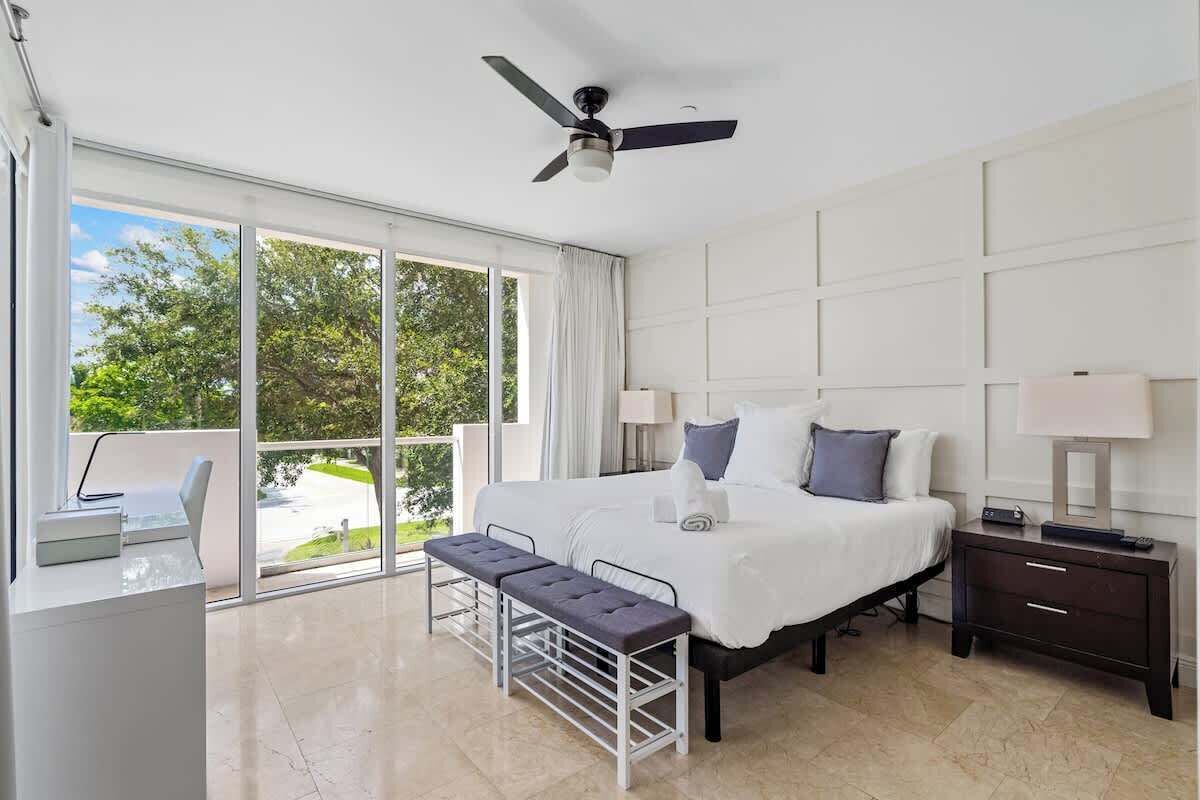 Una habitación de hotel moderna con una cama grande, un escritorio, un banco y un ventilador de techo.