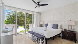 A modern hotel room with a large bed, a desk, a bench, and a ceiling fan. - Hemingway 3 Bedroom Condo 2 Blocks from the Beach (Deerfield Beach)