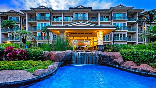 A hotel with a pool, a waterfall, and lush greenery.